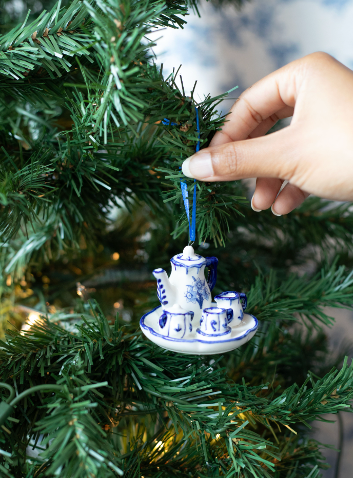 Hand hanging an ornament of a miniature blue and white ceramic tea set.