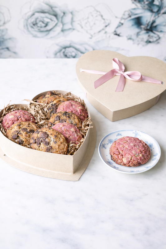 Heart-shaped box of nutty chocolate chip  and white chocolate raspberry rose cookies with a pink ribbon tied on the lid.
