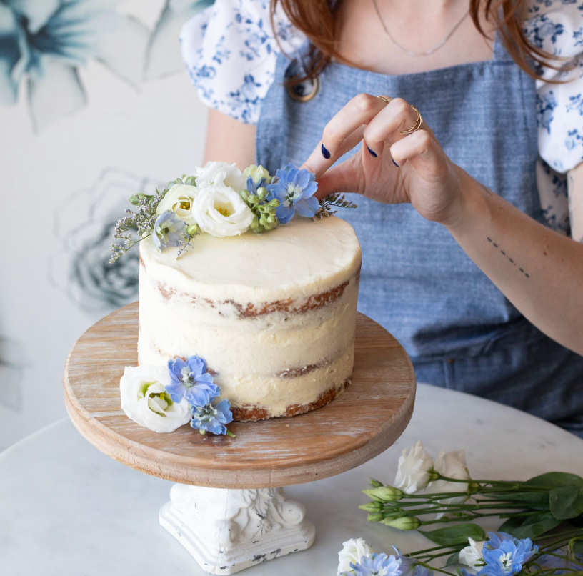 Hand placing blue flowers on a small cake with white icing. 